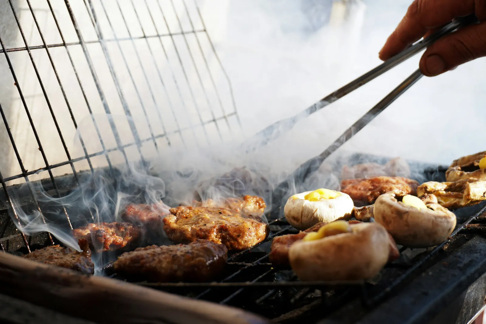 Meat and stuffed mushrooms cooking over a smoking charcoal grill